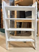 Front view of white 4-shelf wooden bookcase showing all shelves and distressed paint