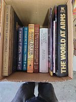 Top-down view of approximately ten assorted hardcover books in a box, showing spines and titles