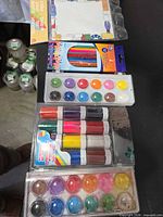 All items laid out: colored pencils, watercolor palette, paint pots, paper pad visible