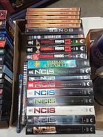 Stacked DVD and Blu-ray box sets and keepcases showing NCIS, Criminal Minds, Bones, Stargate Atlantis, War of the Worlds, San Andreas, Transformers spines