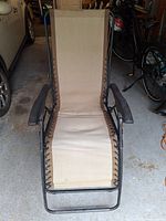 Front view of one zero-gravity chair showing tan sling fabric, black frame, armrests, lacing