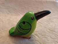 Left side view of green ceramic bird whistle showing sounding hole, painted wing detail and black beak