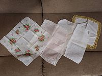 Five hankies on sofa seat showing floral print, pink lace, plain off-white, and yellow-edged examples