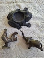 Frog tealight holder, rooster and elephant figurines displayed on fabric background