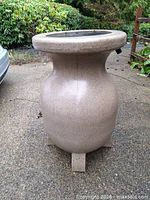 Front view of tan resin rain barrel showing open top and overall shape