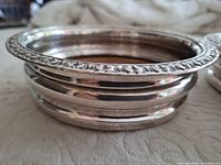 Side profile of one silver-tone coaster showing banded sides and floral rim