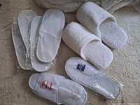Six pairs of assorted white hotel spa slippers displayed on bedspread