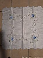 Full view of square white cloth with blue rose embroidery