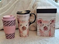 Both travel mugs and gift box visible: pink plastic mug with text, ceramic pig motif mug with lid and handle, matching box
