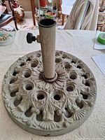 Top view of umbrella stand showing ornate cast metal base, vertical pipe, and tightening knob