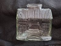 Front view of clear glass house coin bank showing molded windows, door and ribbed roof