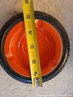 Ceramic tire ashtray with orange interior and tape measure across diameter