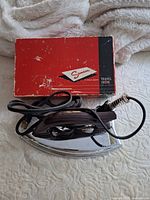 Fold-away travel iron with cord beside original Samson box