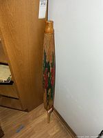 Full view of folded umbrella leaning against wall showing length and multicolour pattern