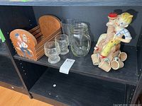 Shelf with wood basket, four glass goblets, glass mason jar mug, ceramic decanter with cups
