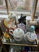 Overall view of shelf showing retirement fund bank, teapots, figures, insulator, tin and box