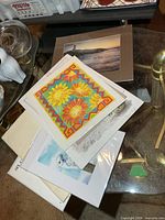 Stack of assorted unframed prints on glass table