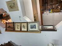 Five framed artworks lined on shelf