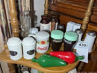Shelf displaying assorted shakers including Coca-Cola, chili peppers, porcelain and glass pieces