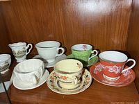 Front view of all cups, saucers, creamer and sugar on shelf