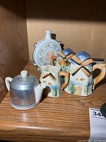 Group shot showing aluminum teapot, two windmill ceramic pieces, porcelain decanter