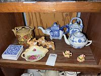 Shelf view showing four teapots, coaster set, miniature teapots, elephants, floral dish
