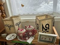 Overall lot on shelf showing both teapots, tray, dishes, fabric covers and framed art