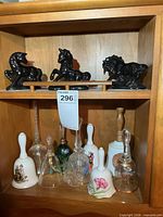Shelf displaying three black pottery unicorns and eight assorted bells