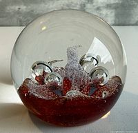 Front view of spherical glass paperweight showing red interior and bubbles