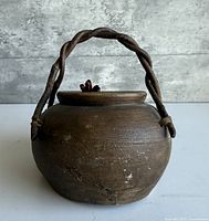 Front view of brown ceramic pot with twisted wood handle and lid