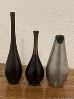 Front view of three metal vases: two dark Japanese vases and one silver-tone Holland vase