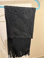 Full view of folded black crochet shawl showing floral lace pattern and fringe