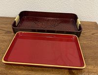 Both trays side by side: deep maroon carved tray behind, red flat tray in front