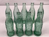 Group shot of nine green glass Coca-Cola contour bottles