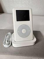 Front view of iPod Classic standing in dock with earbuds beside