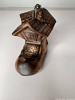 Angled front view of boot house coin bank showing roof, chimney, laced toe and brown finish