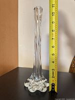 Full view of clear glass bud vase next to tape measure showing height