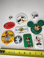 All eleven Disney Mickey Mouse themed pinback buttons displayed with measuring tape for scale