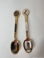 Two gold-tone enamel souvenir spoons side by side