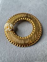 Front view of circular gold-tone brooch with cream resin flower