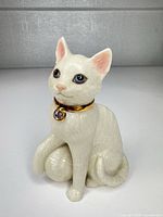 Front view of cream porcelain cat figurine showing gold collar and charm