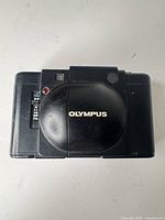 Front view with lens cover closed showing Olympus logo