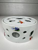 Side view of cylindrical porcelain flower frog showing floral decals and perforations