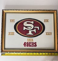 Full view of framed 49ers embroidered fabric art with measuring tape showing width