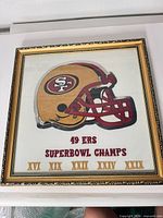 Full view of framed embroidery showing helmet, text, Roman numerals