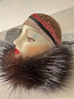 Left profile of brooch showing face, hat trim, fur collar, caliper for scale