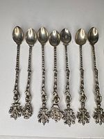 Seven silver-plated ornate demitasse spoons laid out