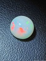 Round opal showing red and green play-of-color on black background