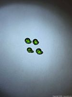 Four round electric green chrome diopside stones under lighting
