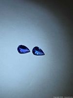 Two pear-cut blue-violet gemstones on light surface